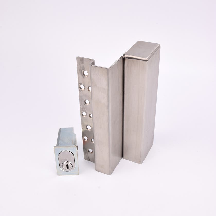 Två metallföremål visas. Det större är en L-formad nyckelförvaringsenhet med flera cirkulära hål längs ena sidan. Det mindre är en rektangulär cylinderhållare med en oval cylinder.