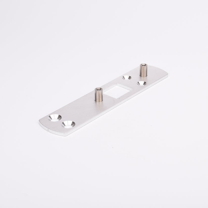 Rektangulär metallplatta med två cylindriska distanser och fyra försänkta hål, symmetriskt placerade. Plattan har även ett rektangulärt urtag i mitten.