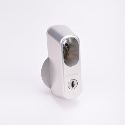 Avlångt silverfärgat låshus med ovalt urtag och nyckelcylinder i nedre delen.