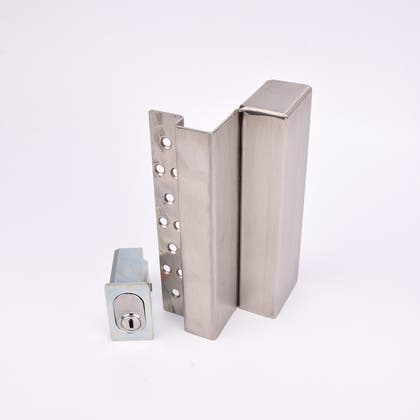 Två metallföremål visas. Det större är en L-formad nyckelförvaringsenhet med flera cirkulära hål längs ena sidan. Det mindre är en rektangulär cylinderhållare med en oval cylinder.