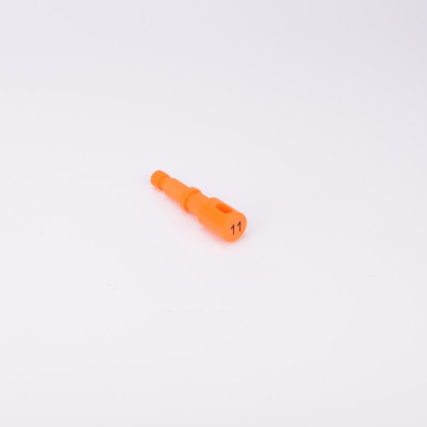 Orange användarpegg med cylindrisk form och flera sektioner med olika diameter. Ena änden är ihålig med ett avlångt spår, medan den motsatta änden har en räfflad yta.