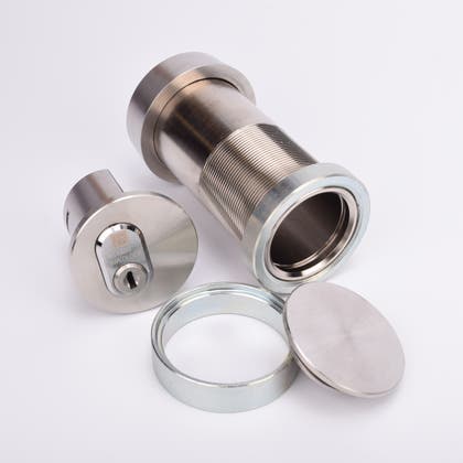 Cylindrisk silverfärgat nyckelfacksrör samt ett runt lås, en rund bricka och en rund ring.