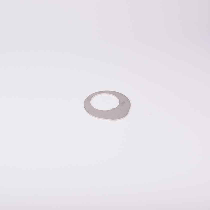 Distansbricka i metall med oregelbunden form och ett centralt hål.
