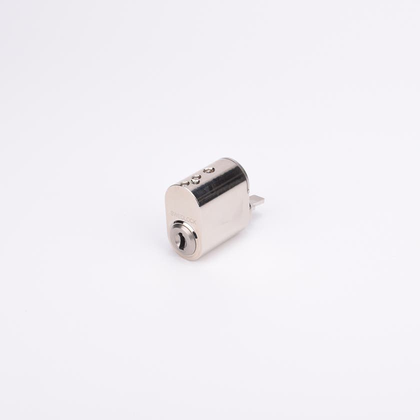 Oval låscylinder i silverfärgad metall med en kort, platt, räfflad metall medbringare.