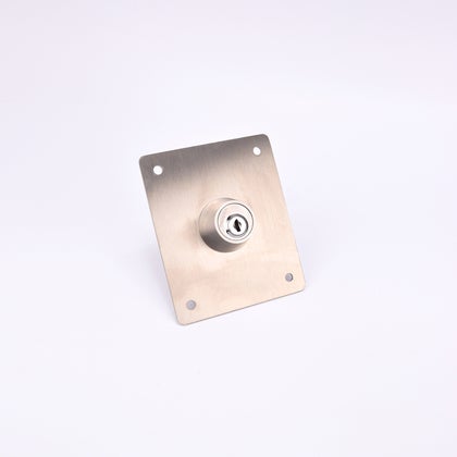 En rektangulär metallplatta med ett cylinderlås i mitten och fyra hål i hörnen.
