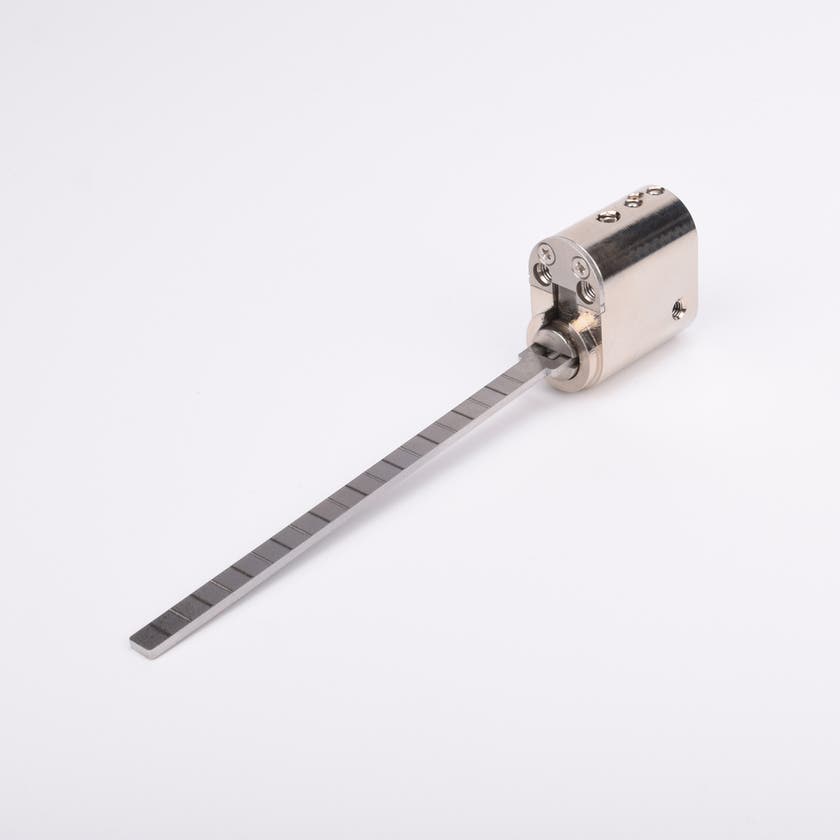 Oval låscylinder i silverfärgad metall med en lång, platt, räfflad metall medbringare.