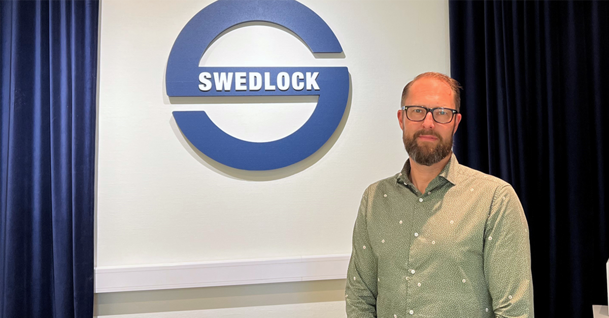 En person framför en vit vägg med en blå Swedlock logga