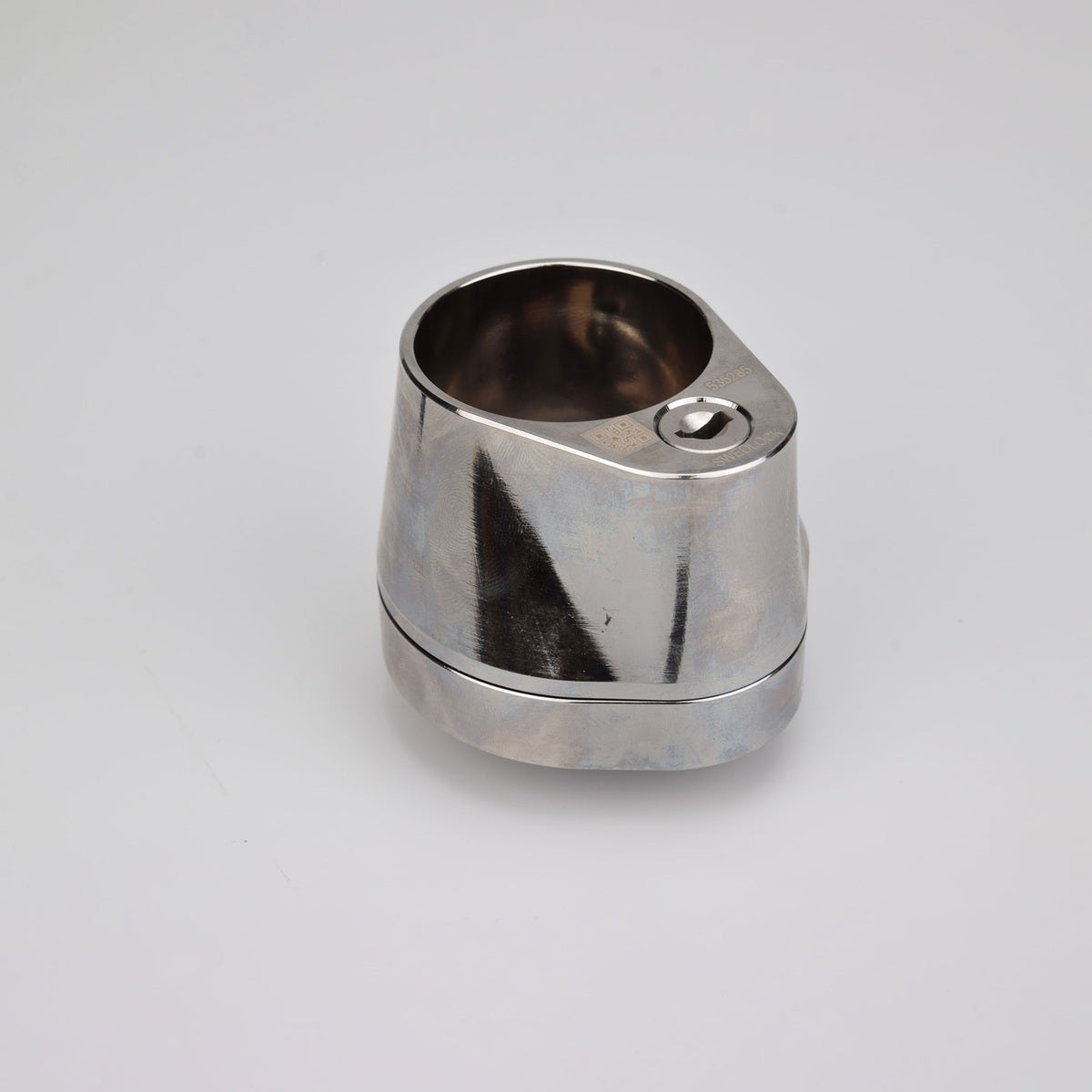 Droppformat metallhus med runt urtag för låscylinder, samt nyckelhål i nedre avsmalnande delen.