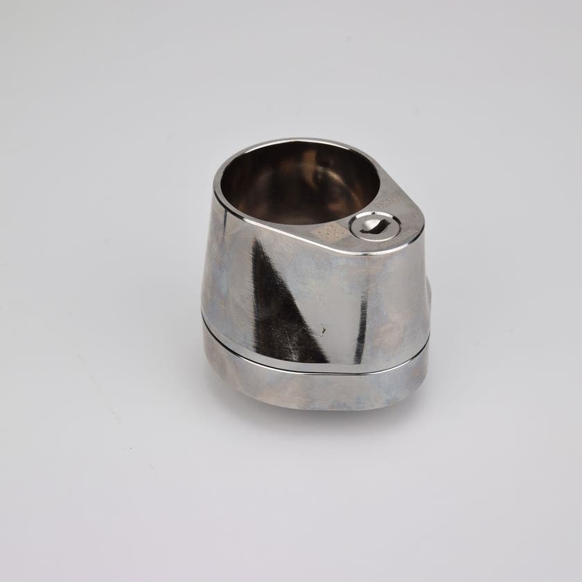 Droppformat metallhus med runt urtag för låscylinder, samt nyckelhål i nedre avsmalnande delen.