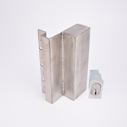 Två metallföremål visas. Det större är en L-formad nyckelförvaringsenhet med flera cirkulära hål längs ena sidan. Det mindre är en rektangulär cylinderhållare med en oval cylinder.