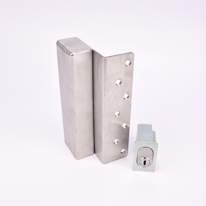 Två metallföremål visas. Det större är en L-formad nyckelförvaringsenhet med flera cirkulära hål längs ena sidan. Det mindre är en rektangulär cylinderhållare med en oval cylinder.