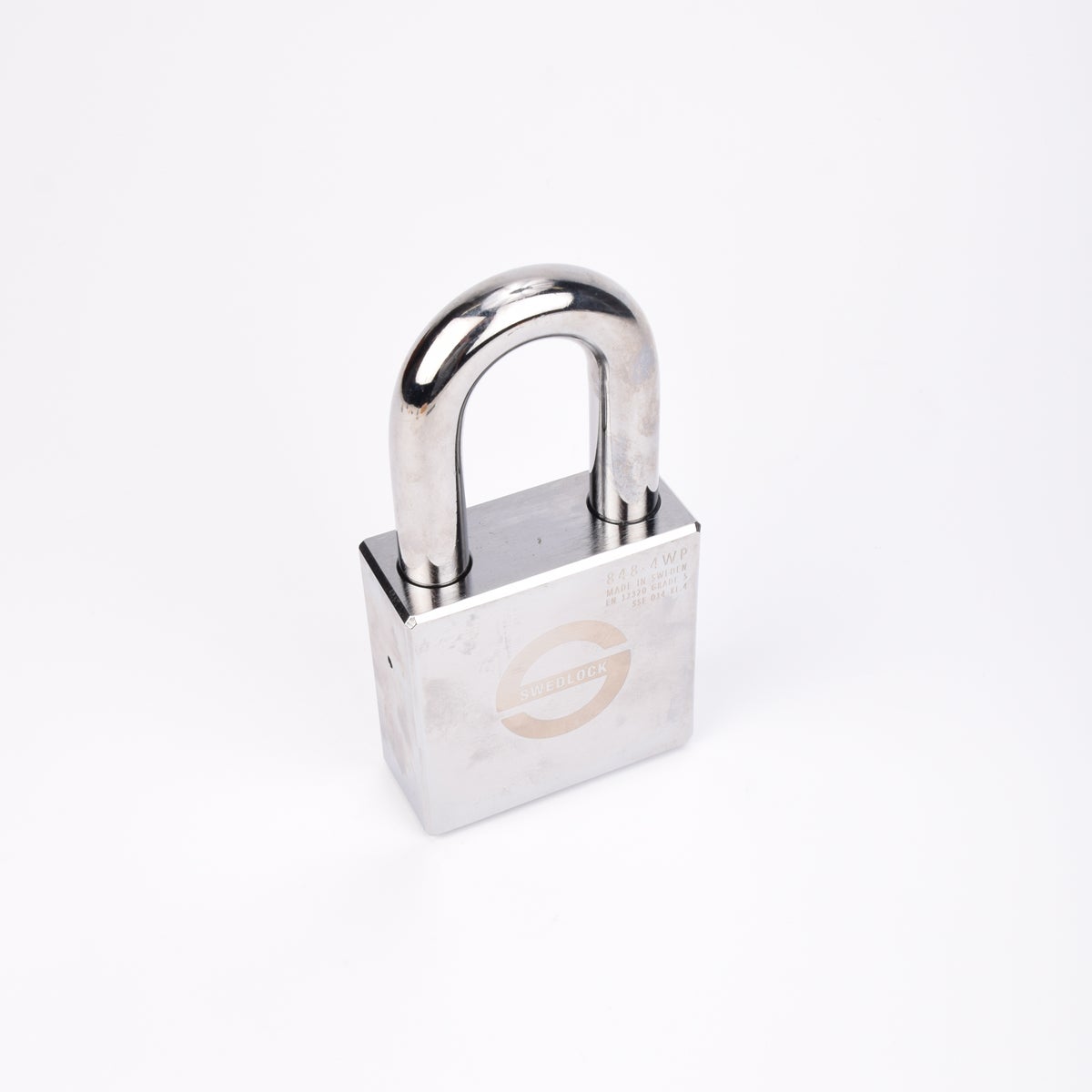 Silverfärgat Svedlock‑hänglås i metall med rund, robust bygel och graverad märkning på framsidan.