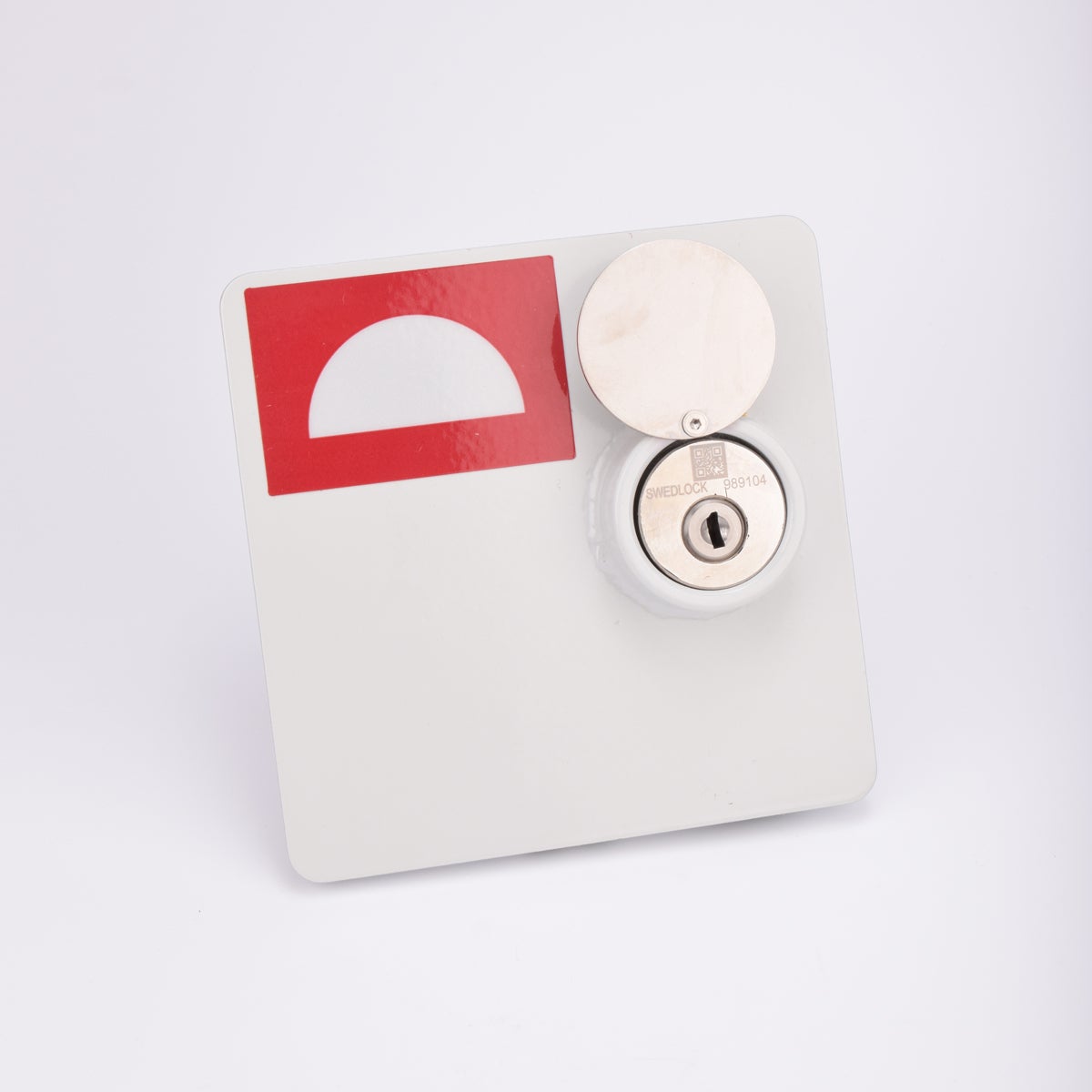 En vit fyrkantig brandlucka, med en rektangulär röd dekal i vänstra hörnet. Luckan har ett metalliskt lås med nyckelhål.