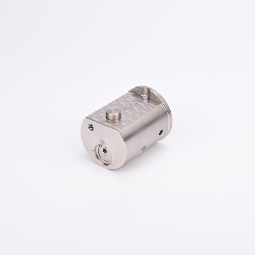 Metallisk cylindrisk komponent med platt topp och botten, försedd med hål och urtag.