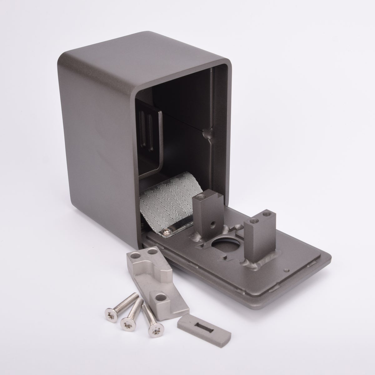 Grått fasadnyckelskåp i metall med rundade hörn, luckan är i öppet läge och framför skåpet ligger tre skruvar och två metallbitar.