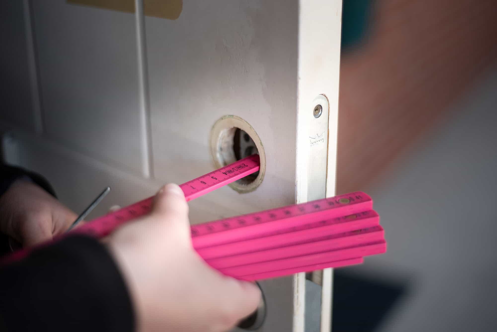 Händer som mäter ett dörrmått med en rosa måttstock