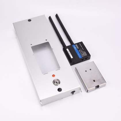 Tre komponenter till elektronisk låsenhet: metallplatta med nyckelhål, svart modul med antenner och etiketter, samt fyrkantigt metallhölje med två hål.