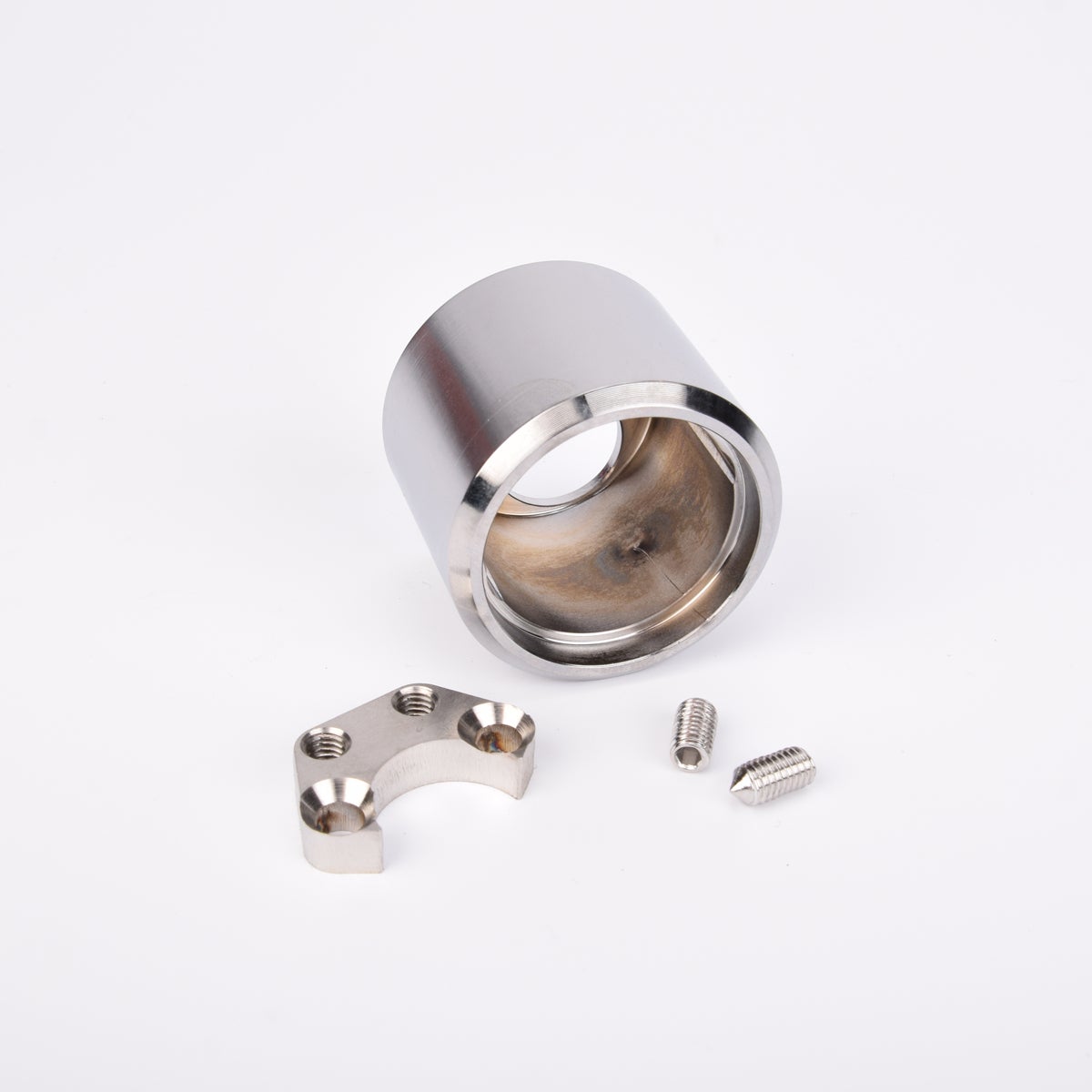 Cylinderformad metallkomponent med central öppning, bågformad del och två små skruvar.