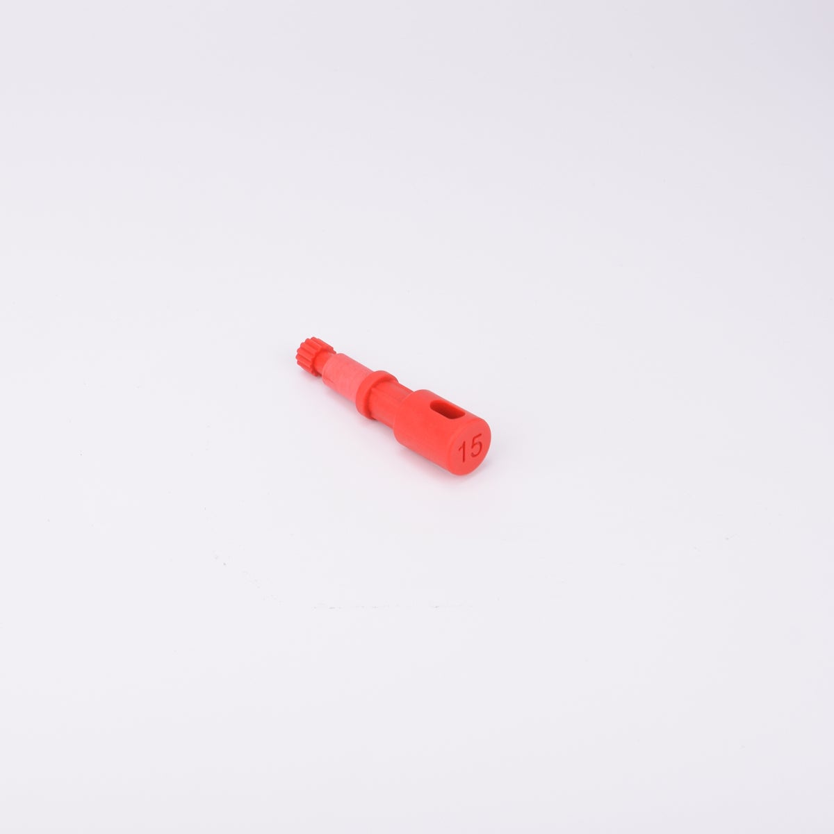 Röd användarpegg med cylindrisk form och flera sektioner med olika diameter. Ena änden är ihålig med ett avlångt spår, medan den motsatta änden har en räfflad yta.
