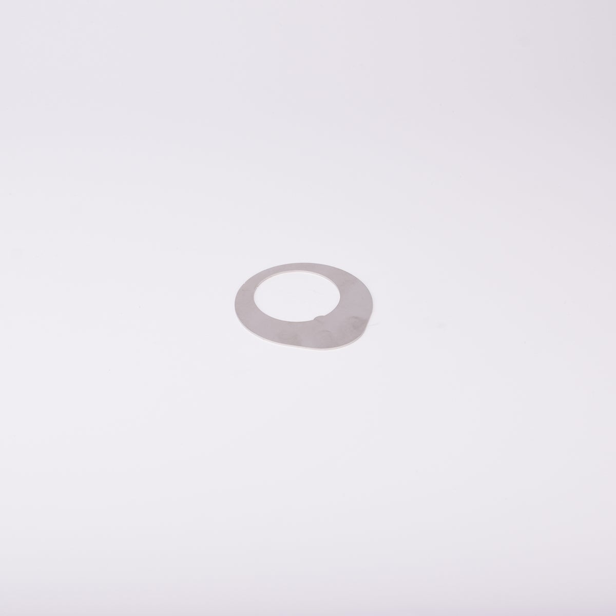 Distansbricka i metall med oregelbunden form och ett centralt hål.