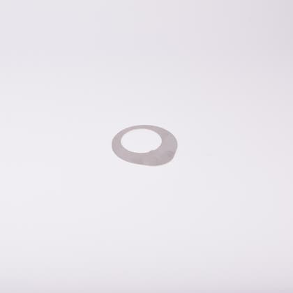 Distansbricka i metall med oregelbunden form och ett centralt hål.