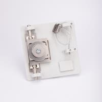 Metallkomponent monterad på vit bas med centralt bultfäste, två cylindrar, trådögla och klämmor.