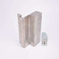 Två metallföremål visas. Det större är en L-formad nyckelförvaringsenhet med flera cirkulära hål längs ena sidan. Det mindre är en rektangulär cylinderhållare med en oval cylinder.