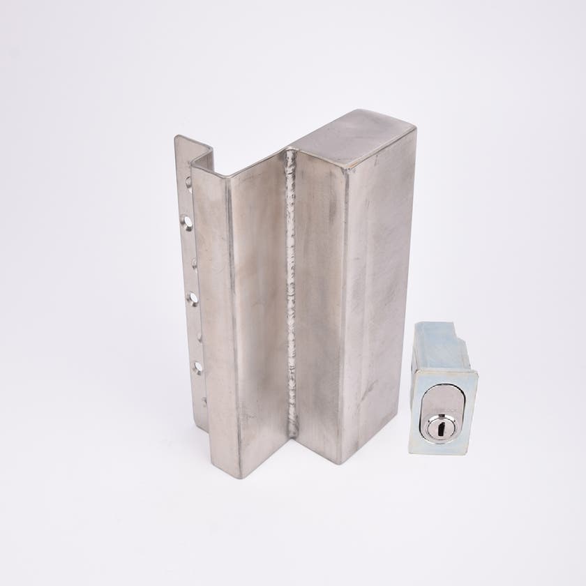 Två metallföremål visas. Det större är en L-formad nyckelförvaringsenhet med flera cirkulära hål längs ena sidan. Det mindre är en rektangulär cylinderhållare med en oval cylinder.