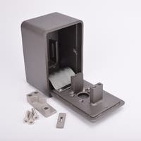 Grått fasadnyckelskåp i metall med rundade hörn och helt utfälld lucka, samt metallkomponenter och skruvar liggandes utanför.