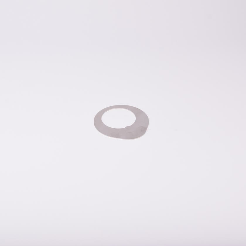 Distansbricka i metall med oregelbunden form och ett centralt hål.