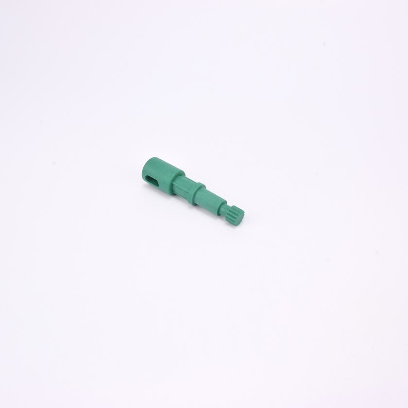 Grön användarpegg med cylindrisk form och flera sektioner med olika diameter. Ena änden är ihålig med ett avlångt spår, medan den motsatta änden har en räfflad yta.