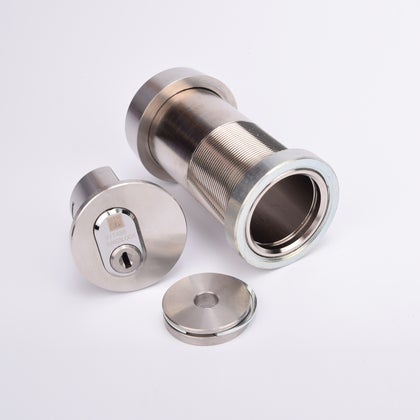 Isärtaget cylindriskt nyckelfacksrör med gängad hylsa, låsmekanism med nyckelhål, samt en rund metallkåpa.