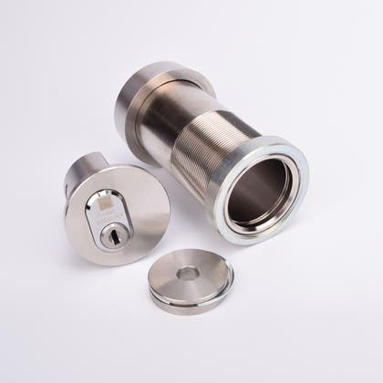 Isärtaget cylindriskt nyckelfacksrör med gängad hylsa, låsmekanism med nyckelhål, samt en rund metallkåpa.