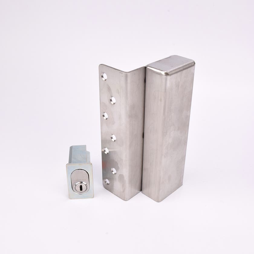 Två metallföremål visas. Det större är en L-formad nyckelförvaringsenhet med flera cirkulära hål längs ena sidan. Det mindre är en rektangulär cylinderhållare med en oval cylinder.