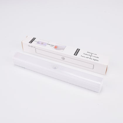 Vit LED-lampa med rörelsesensor, liggande framför sin förpackning.