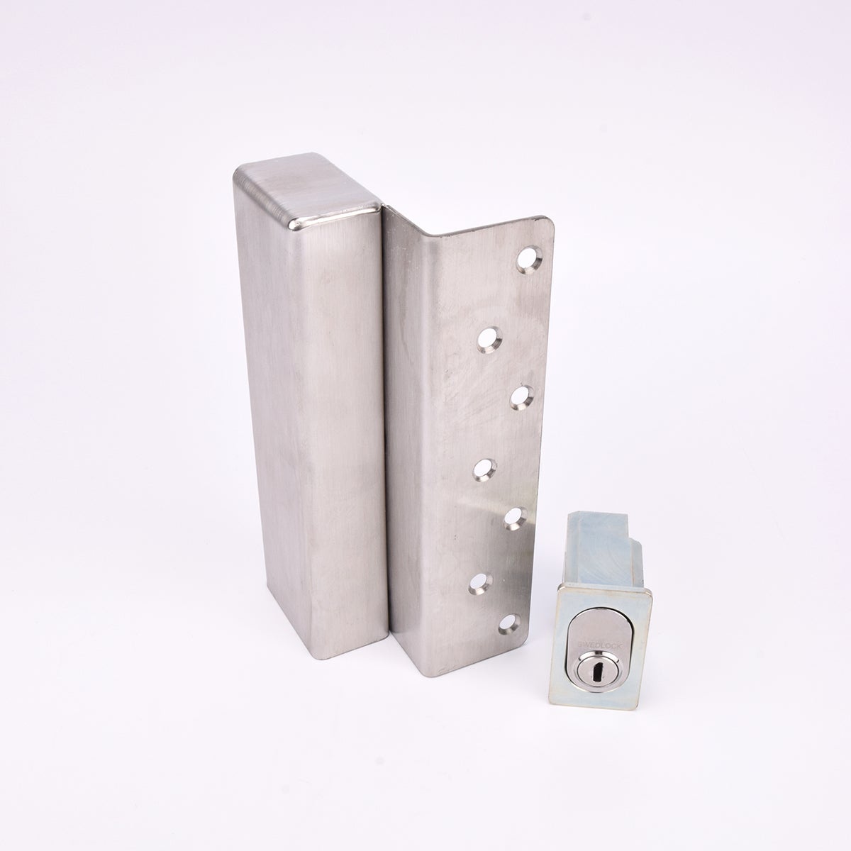 Två metallföremål visas. Det större är en L-formad nyckelförvaringsenhet med flera cirkulära hål längs ena sidan. Det mindre är en rektangulär cylinderhållare med en oval cylinder.