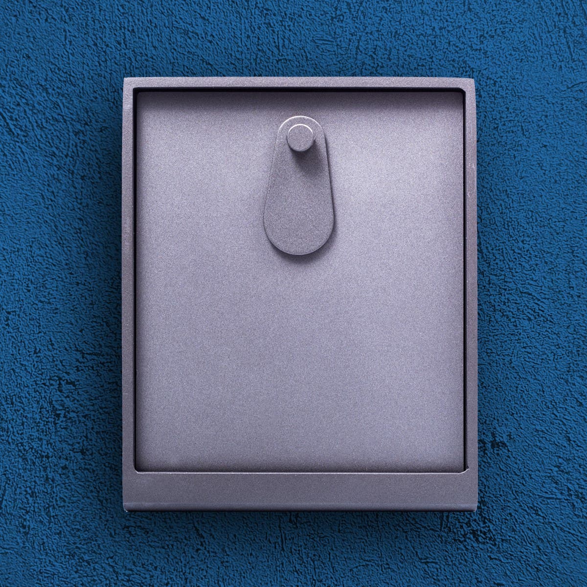 Fyrkantigt grått skåp mot en mörkblå bakgrund.