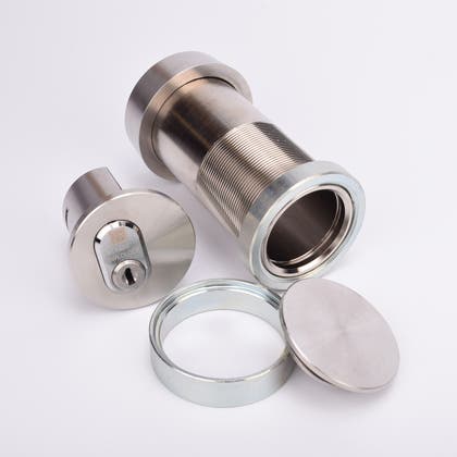 Cylindrisk silverfärgat nyckelfacksrör samt ett runt lås, en rund bricka och en rund ring.