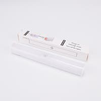 Vit LED-lampa med rörelsesensor, liggande framför sin förpackning.