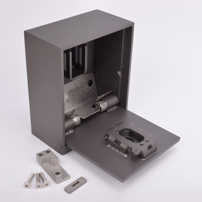 Grått fasadnyckelskåp i metall, luckan är i öppet läge och framför skåpet ligger tre skruvar och två metallbitar.