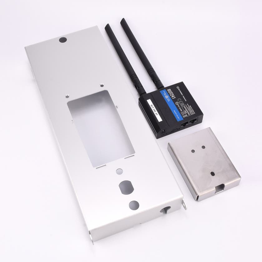 Rektangulär metallhållare med ett stort hål i mitten, samt en svart elektronisk 4G modem.