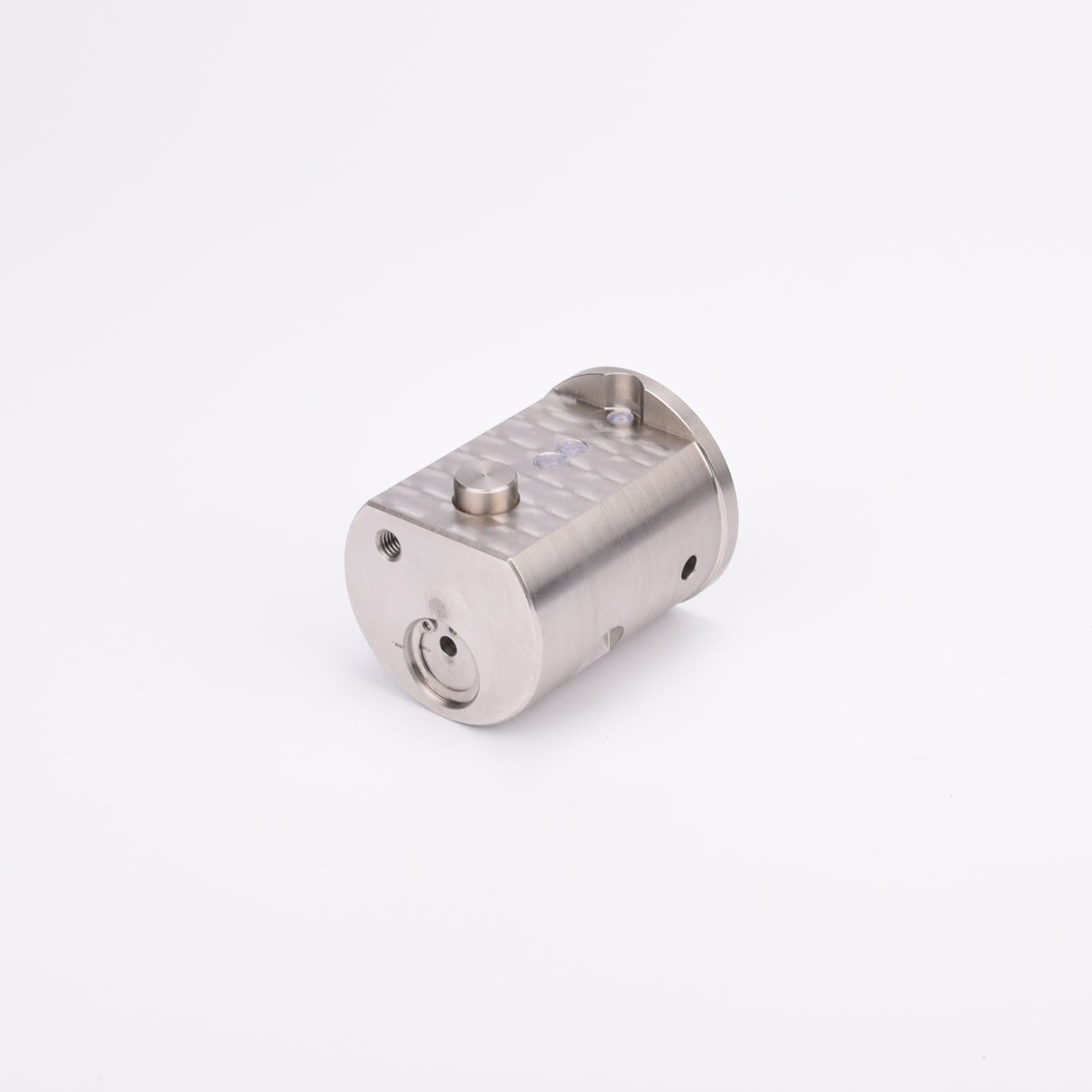 Metallisk cylindrisk komponent med platt topp och botten, försedd med hål och urtag.