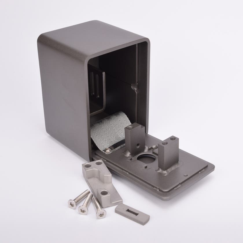 Grått fasadnyckelskåp i metall med rundade hörn, luckan är i öppet läge och framför skåpet ligger tre skruvar och två metallbitar.