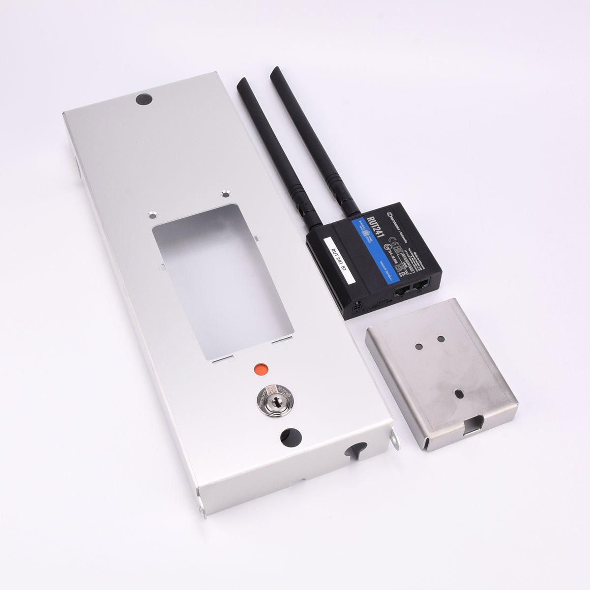 Tre komponenter till elektronisk låsenhet: metallplatta med nyckelhål, svart modul med antenner och etiketter, samt fyrkantigt metallhölje med två hål.