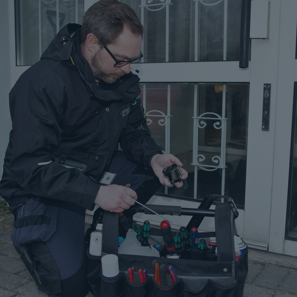 En mann som sitter foran en inngangsdør med en verktøykasse