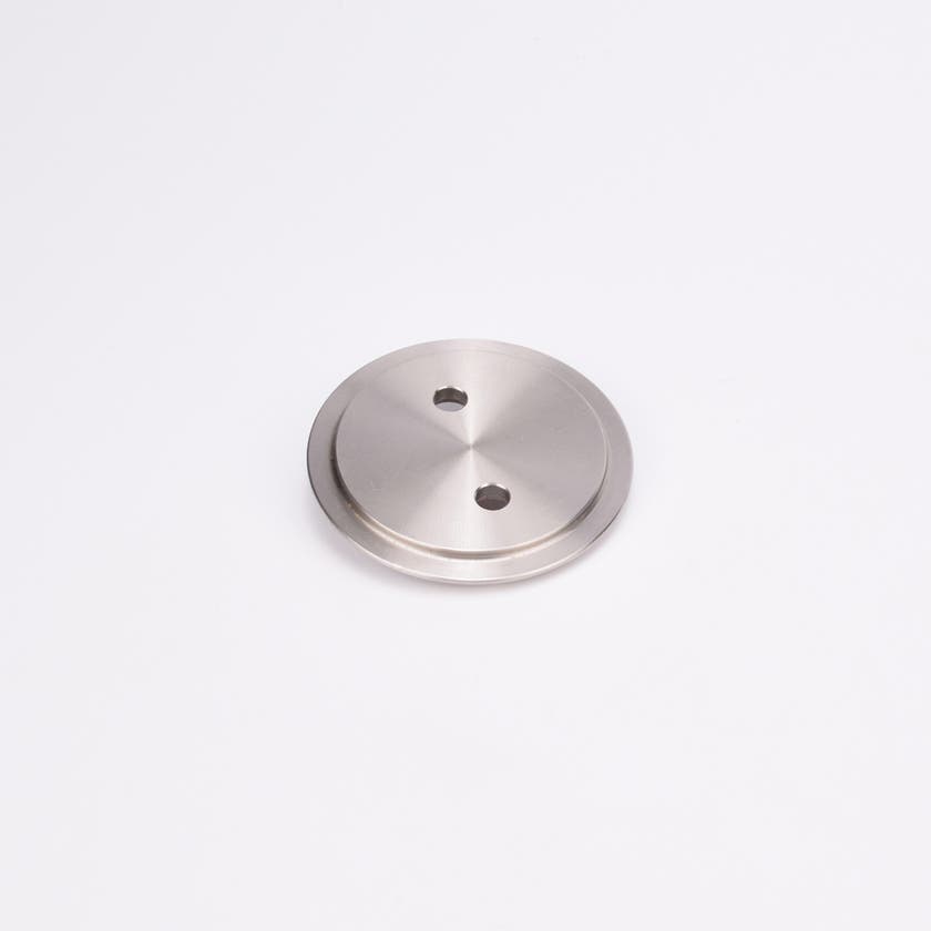 Metallisk, cirkulärt täcklock med slät, reflekterande yta och två jämnt placerade hål nära mitten.