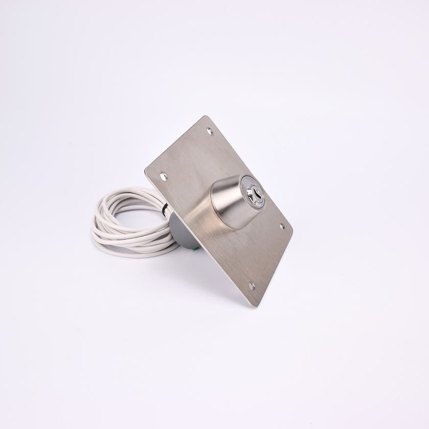 En rektangulär metallplatta med ett cylinderlås i mitten och fyra hål i hörnen, samt en ihoprullad vit kabel.