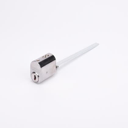 Oval låscylinder i silverfärgad metall med en lång, platt, räfflad medbringare i metall.