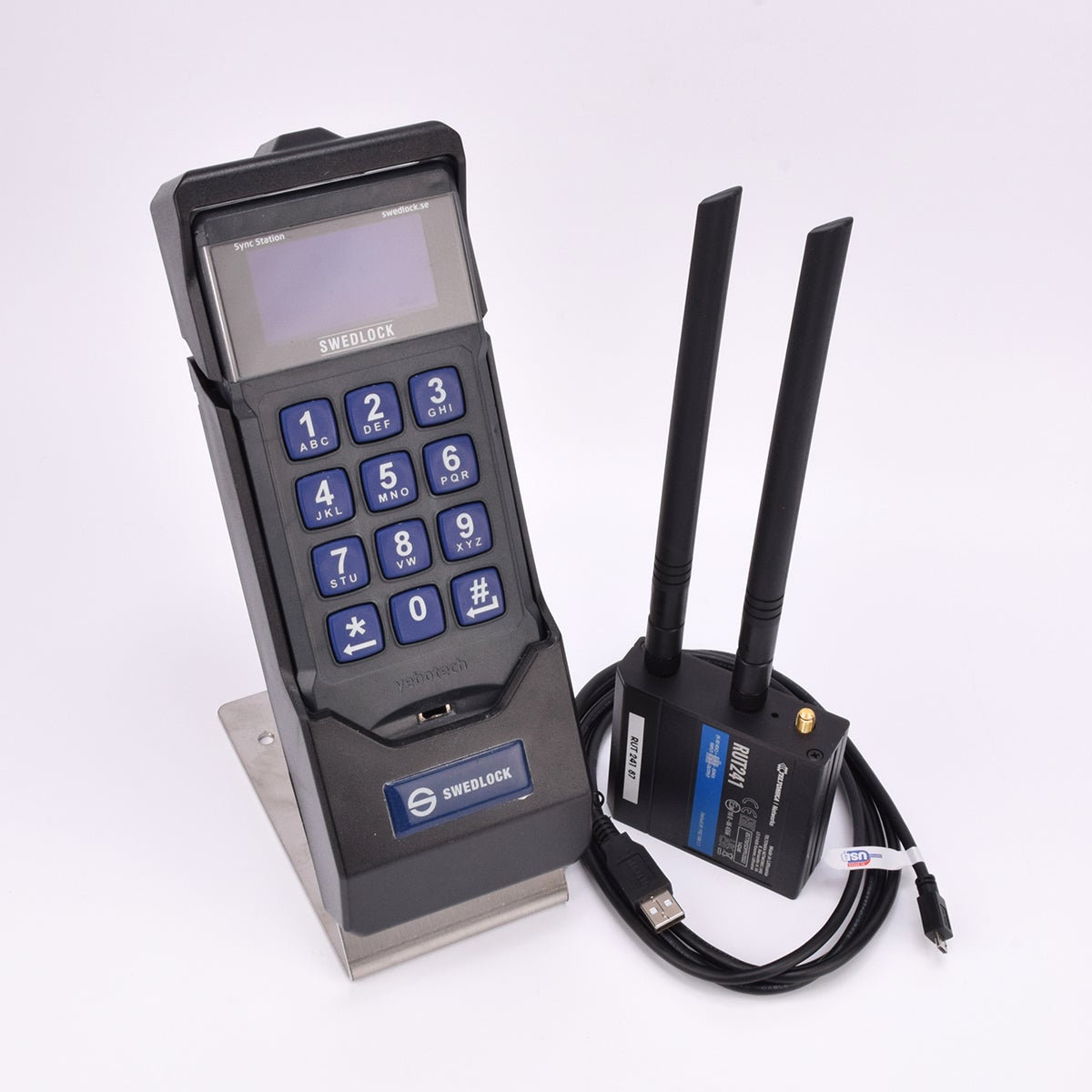 En synkstation med elektronisk knappsats med display, bredvid en svart låda med två antenner och en svart ihoprullad kabel.