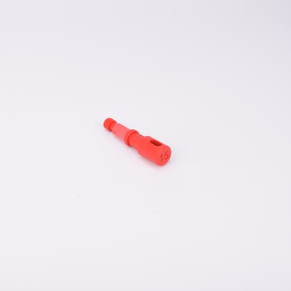 Röd användarpegg med cylindrisk form och flera sektioner med olika diameter. Ena änden är ihålig med ett avlångt spår, medan den motsatta änden har en räfflad yta.